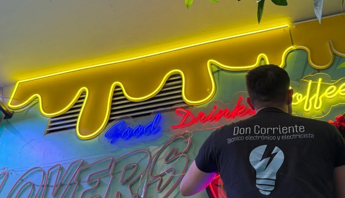 Adrián, de espaldas con la camiseta de Don Corriente, conectando el rótulo de neón de una cafetería